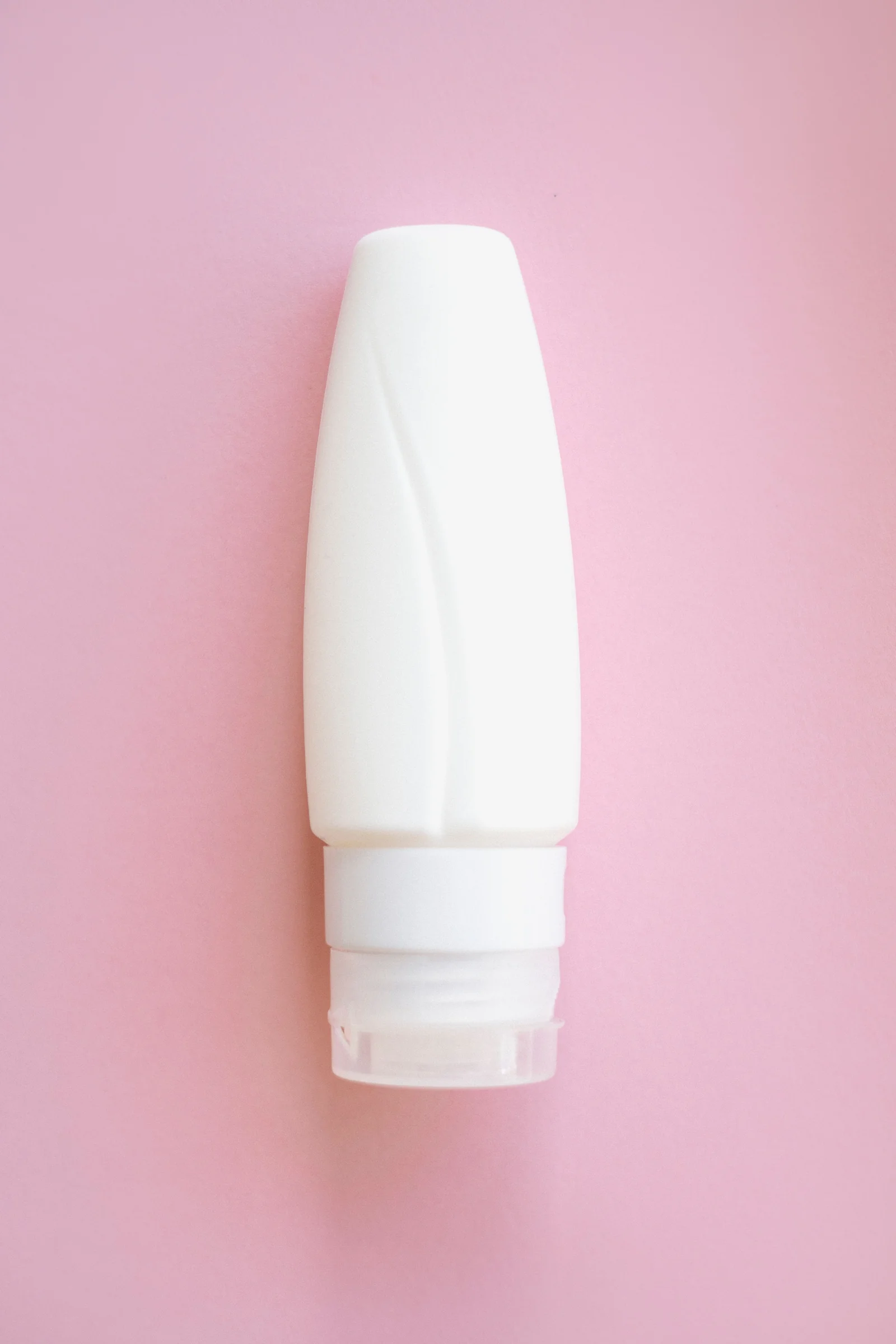 A simple white cosmetic bottle on a soft pink background
