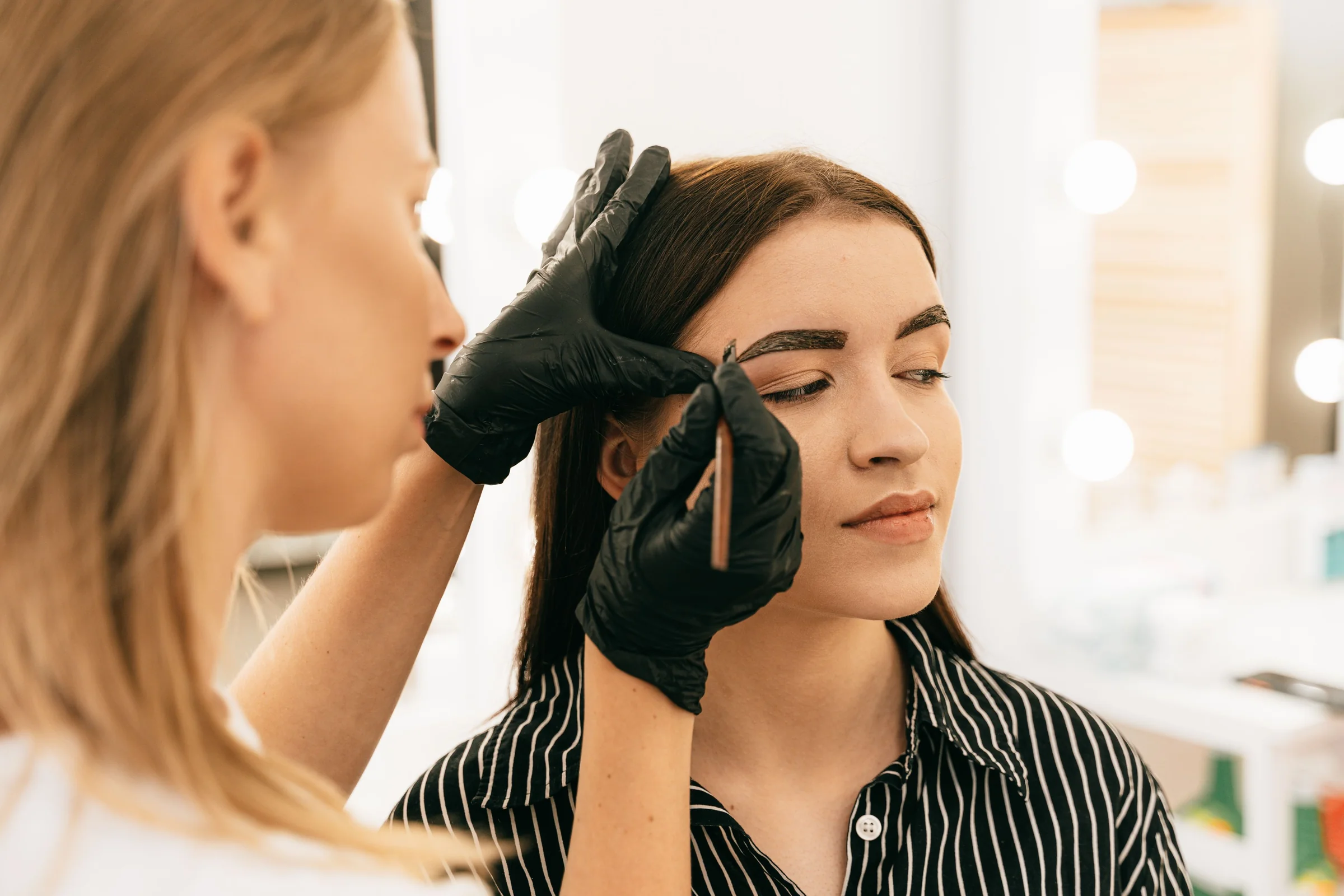 A brow artist in black gloves shaping a woman's eyebrows
