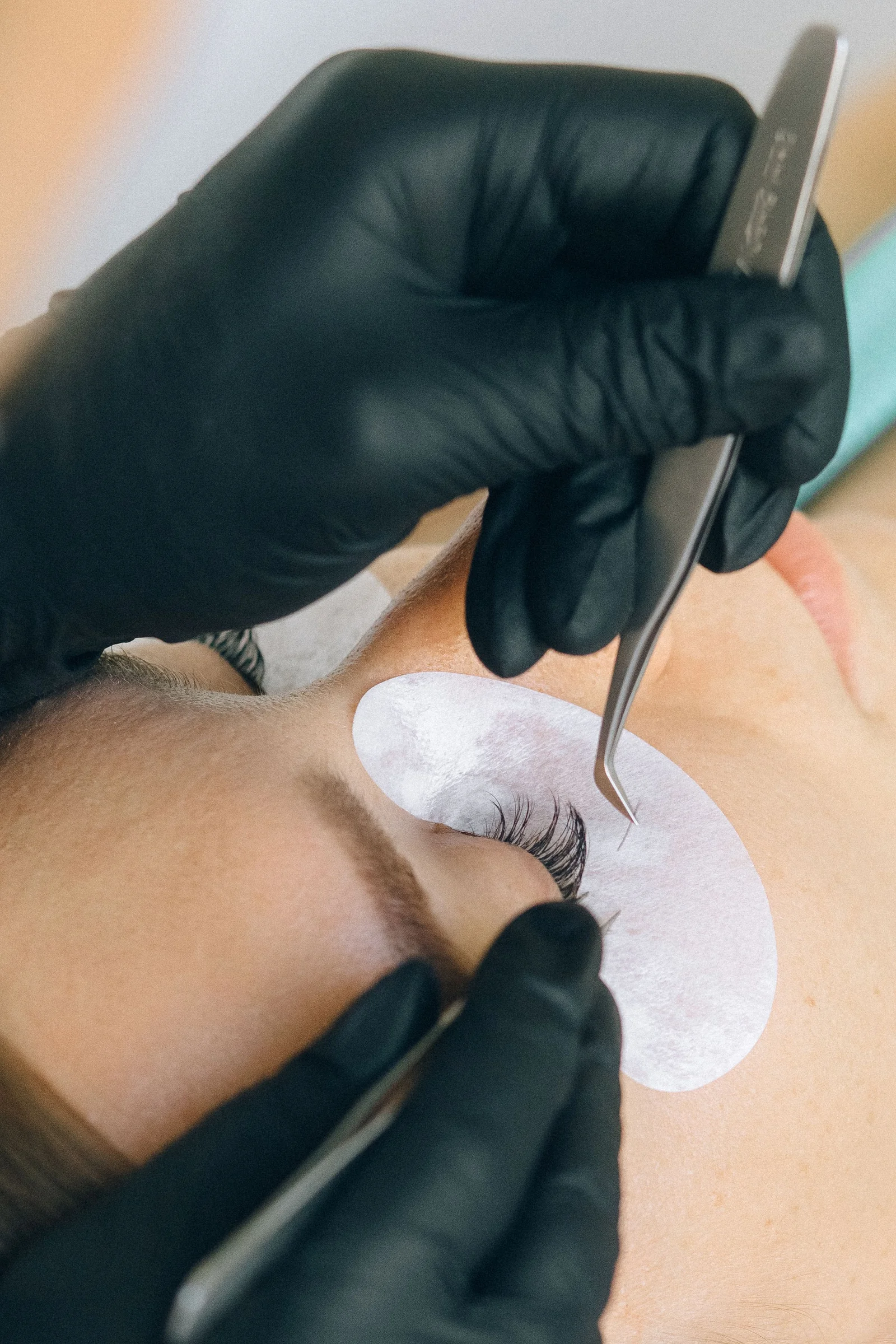 A black-gloved lash artist placing eyelash extensions with tweezers