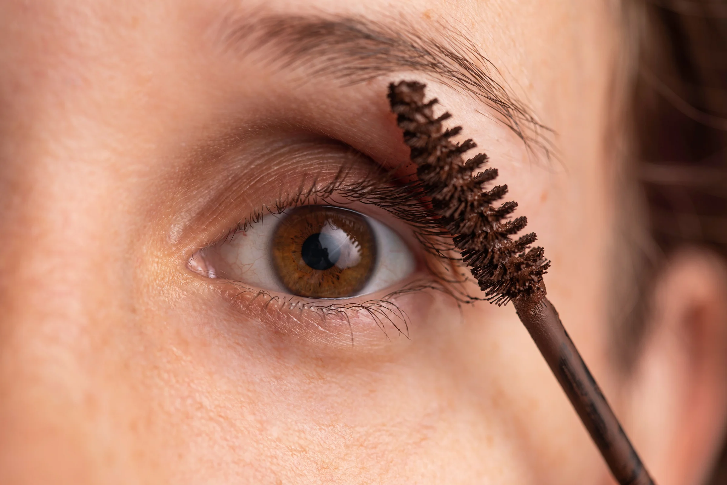Close-up of a brown eye as a spoolie brushes through the lashes