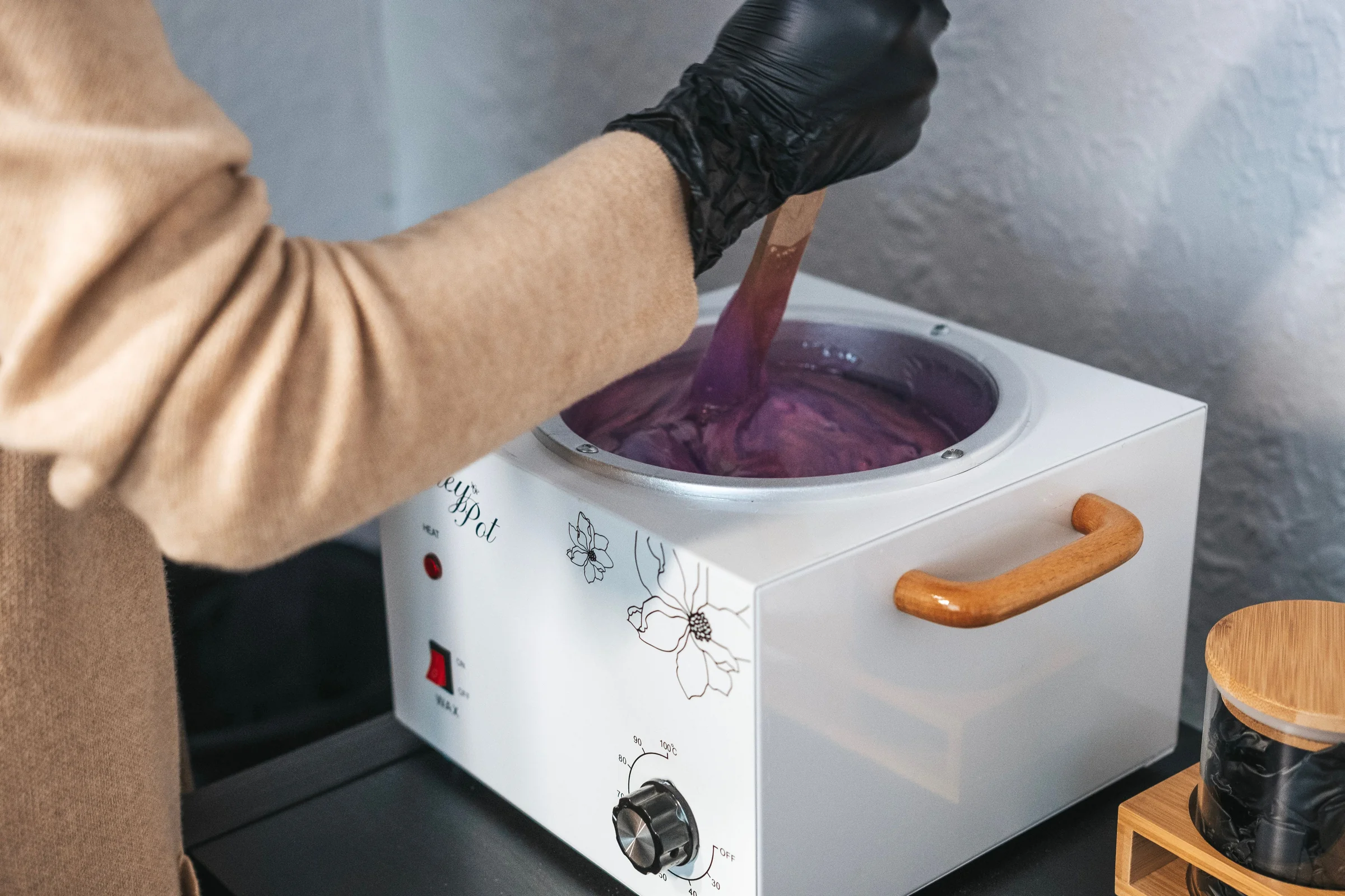 A black-gloved hand stirring warm wax in a wax warmer